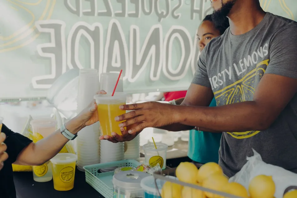 A lemonade vendor handing a freshly poured drink to a customer