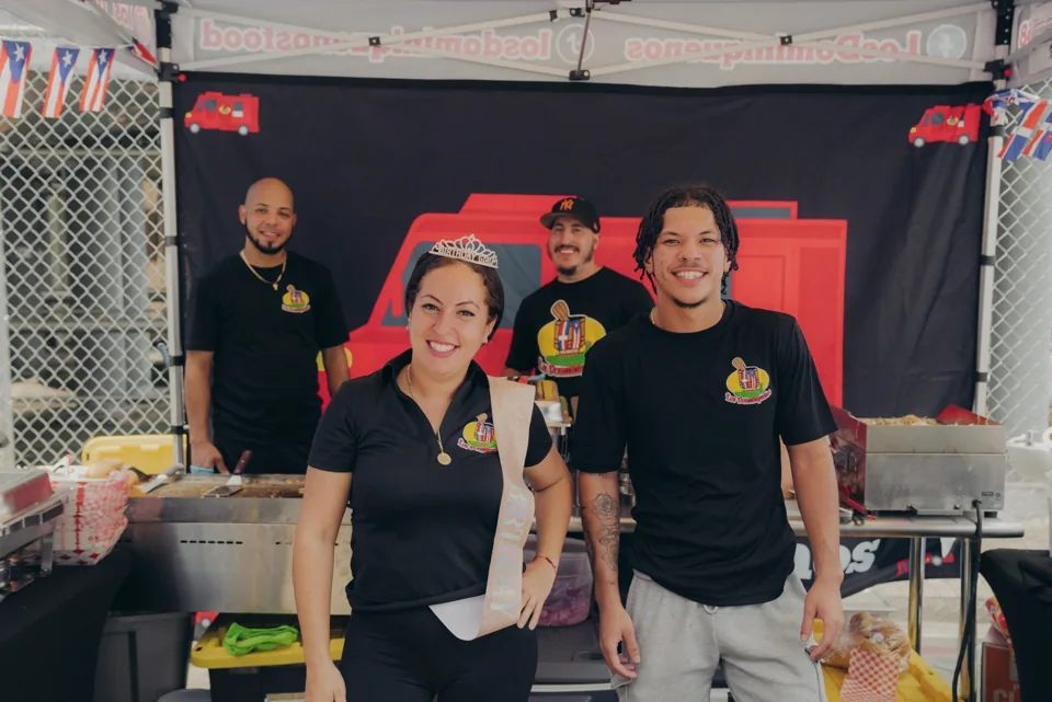 A smiling vendor team standing together at their Sazón food booth