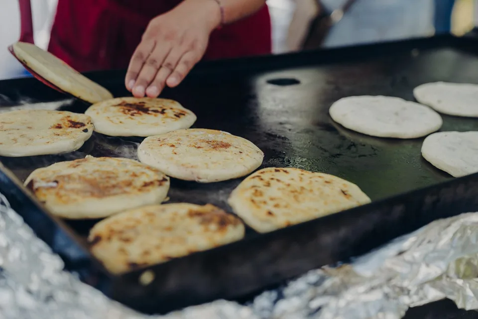 A vendor cooking handmade pupusas on a hot griddle